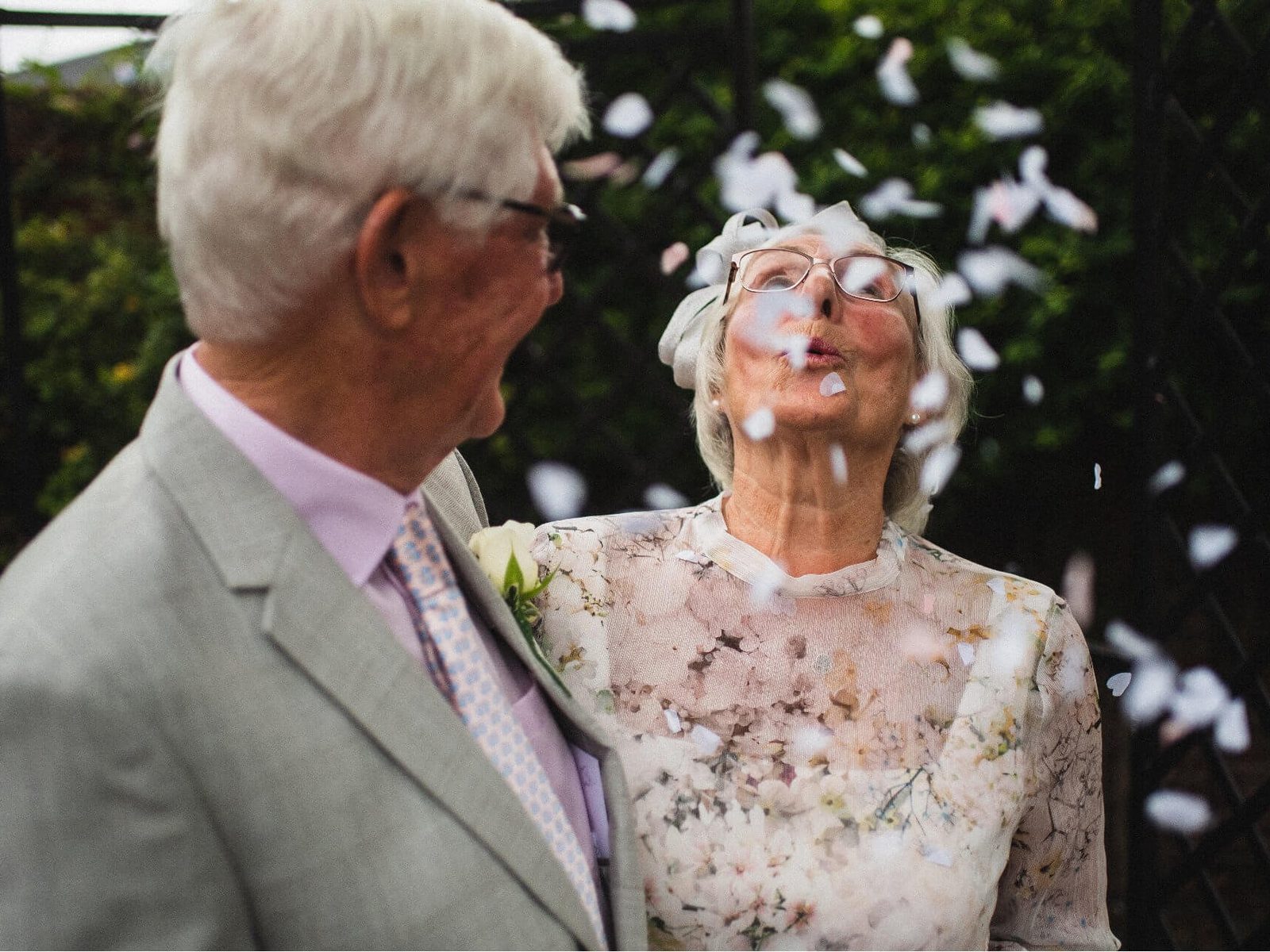 An older couple in their wedding outfits, laughing as confetti falls around them