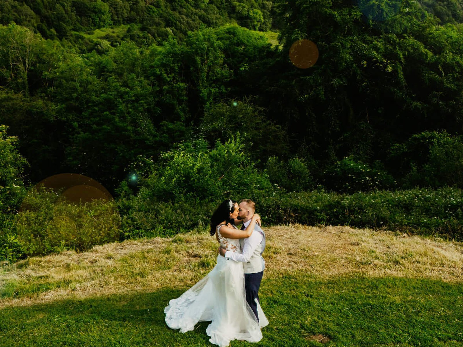 A bride and groom embracing on a grassy hillside in evening sun