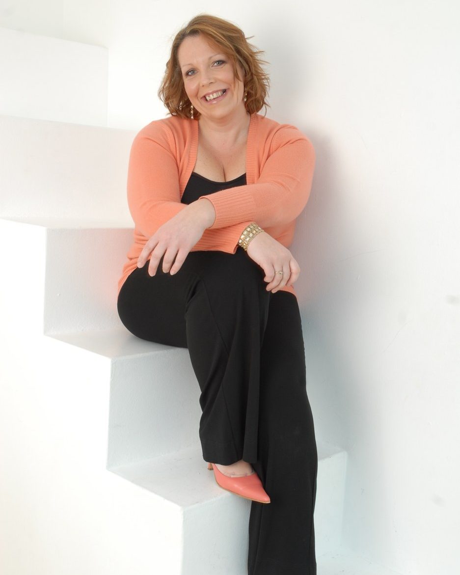 Sara Eastham, celebrant and singer, smiling as she sits on a white staircase