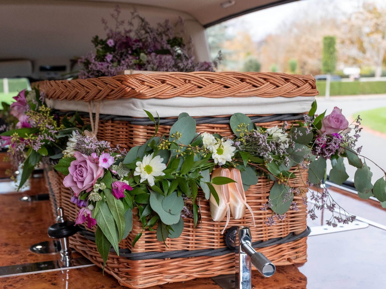 A woven willow coffin dressed with garden flowers and a pair of ballet shoes